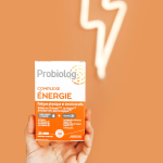 Une main tient Probiolog Complexe Energie dans un fond orange avec un eclair en néon derrière