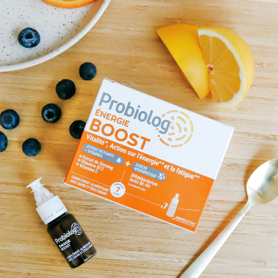 Complément alimentaire Probiolog Energie Boost sur une table avec un shot de Energie Boost, des quartiers d'orange et des myrtilles